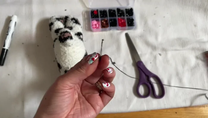 Add finishing touches. Attach the black beads for eyes, nose, and mouth. Sew on the whiskers.