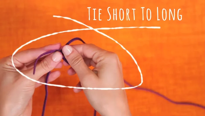 Tie the straps together: Tie the shorter leather strap (with feathers and bead) to the longer leather strap (attached to the yarn ball).