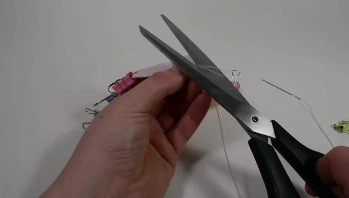 Align the two thread ends, create a knot, and leave about 1/8 inch of thread after the knot. From the backside at the top right, pull the needle down through the fold and back up.