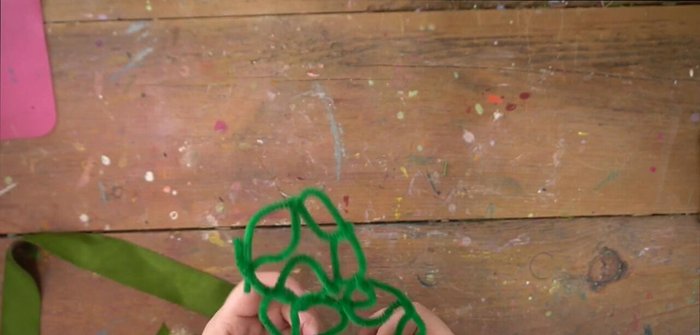 Glue the greenery onto the ribbon-covered framework, starting with larger pieces to fill in gaps and provide a base for smaller details.