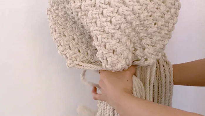 Gather all the bottom cords and tie a simple knot to secure them. Place a square pillow (or similar object) inside the hammock to create shape. Tie a gathering knot at the bottom, using a separate 3-foot cord wrapped around 7 times to create a secure closure. Trim excess cord.