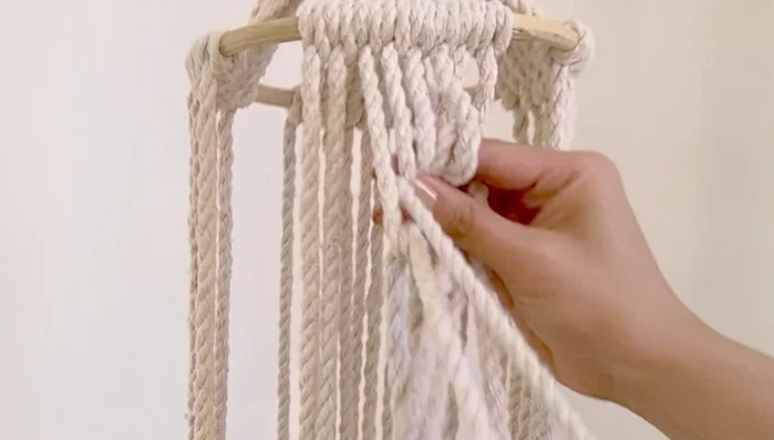 Make square knots with the four middle cords of each section, then use two cords on each side to create additional square knots, using the same middle cords as before. Repeat this process, creating what the presenter calls a 'fishbone' pattern.