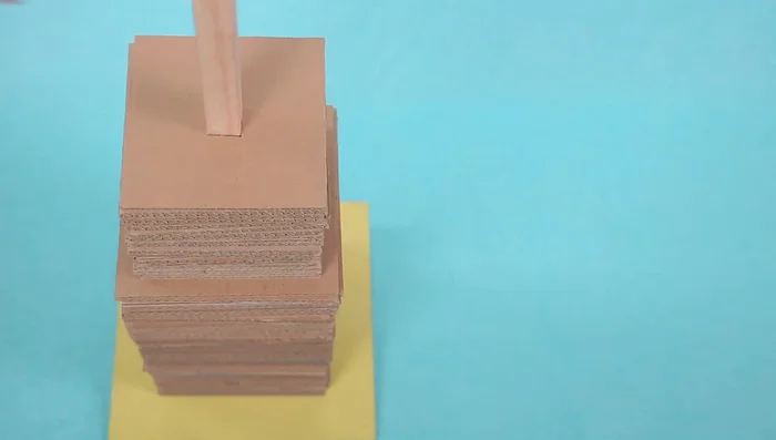 Stack the cardboard squares onto the dowel, starting with the largest and working to the smallest.