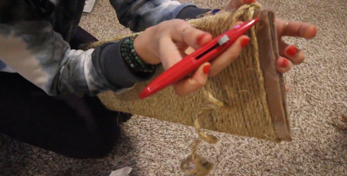 Finish wrapping. Leave about an inch of space at the top. Poke holes in the top corners and thread the sisal rope through. Secure the ends with packing tape for a clean finish.