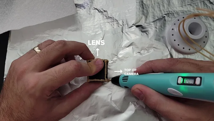 Build vertical supports: Draw two short lines (one cm and two cm) from the back and front right corners of the camera cage, respectively, onto the aluminum foil. Repeat on the other side. Smooth any sharp edges with the pen tip.
