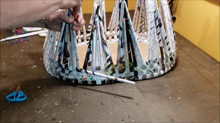 Continue weaving additional rows until the desired height is reached. Trim excess vertical tubes, leaving about a half inch above the final row, and cover with additional strips of rolled magazine paper.