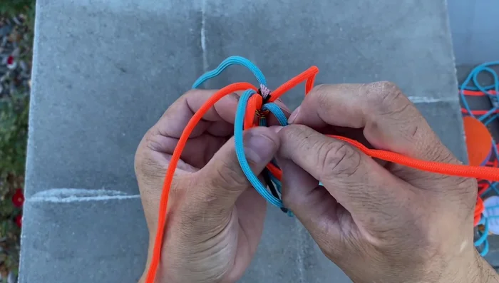Create the hexagon: Start with the orange cord, create a series of overlapping loops, alternating colors (orange over blue, blue over orange). Pass the last blue cord through the initial loop to secure the pattern.