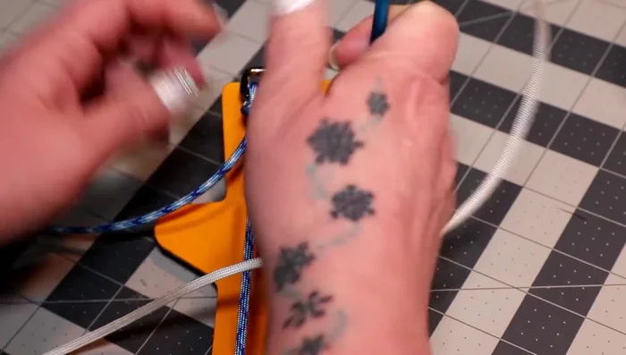 Pull the ends of the white cord down the loop, creating another cow hitch. Before tightening, add the colonial blue cord through the white cow hitch, bringing the middle to the top. Tighten everything.