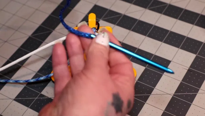 Pull the ends of the white cord down the loop, creating another cow hitch. Before tightening, add the colonial blue cord through the white cow hitch, bringing the middle to the top. Tighten everything.