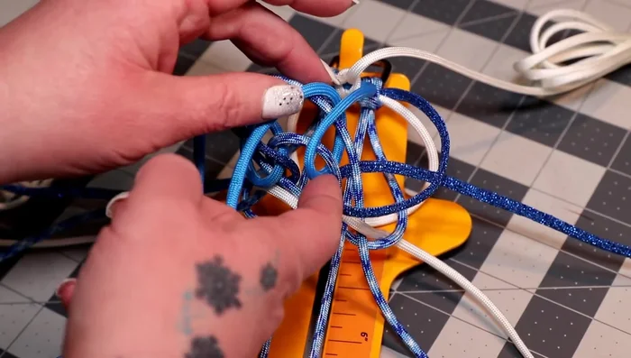 Weave the larger white bundle over the horizontal pieces to the right of the colonial blue, coming up between the white and colonial blue. Repeat on the left side.