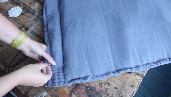 Use a pink embroidery thread to do running stitch all around the pillowcase. Add decorative stitches to the sides, ensuring the needle goes through all layers for a quilted effect.