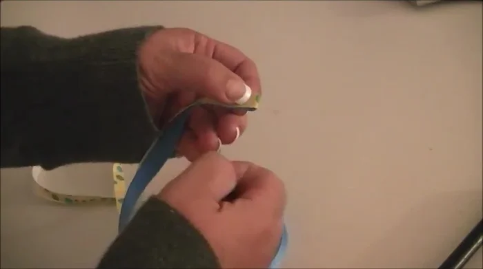 Fold over the ribbon and tack it in place. Sew it down using a quick zig-zag stitch, followed by a straight stitch all the way down, tucking the end of the ribbon under the webbing for a clean finish.