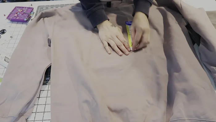 Choose and mark the sweatshirt. Decide on the pocket's placement and size on the sweatshirt. Mark the desired location with pins.