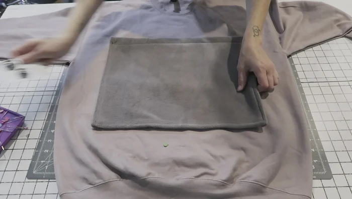 Pin the pocket to the sweatshirt. Pin the finished pocket onto the marked area of the sweatshirt, ensuring even placement on both sides. Avoid pinning through the back of the sweatshirt.