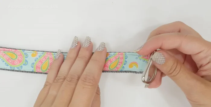 Attach handle. At the other end, slip on a D-ring (optional, skip if not making treat bag). Fold over 7 1/2 inches, ensuring raw edges align with the swivel hook. Fold under a quarter inch and stitch across multiple times. Stitch the D-ring securely into its own pocket.