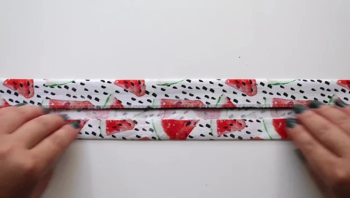 Sew the fabric onto the strap. Tuck the strap under the 1-inch fold, fold the other side of the fabric over to cover the strap completely, and sew around the entire piece, ensuring the edges are tucked in at the ends. Use binder clips to hold the fabric in place while sewing.