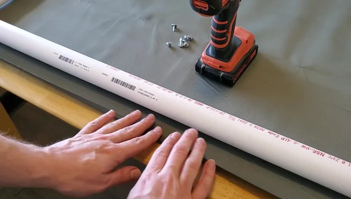 Attach the fabric: Begin by folding the fabric edge over to create a lip and securing the middle with a screw. Then, work down the long sides, stopping before the corners to fold the fabric around the fittings. Repeat for the opposite long side.