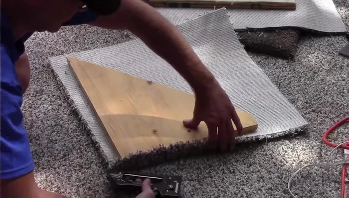 Cover the shelf with carpet, using hot glue and staples. Ensure a one-inch overhang for a clean finish.