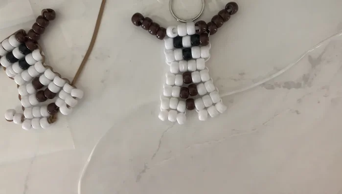 Create the tail: String two white beads onto one string. Thread the string through only *one* of the beads, creating a small loop. Tie off the remaining strings securely to complete the keychain.