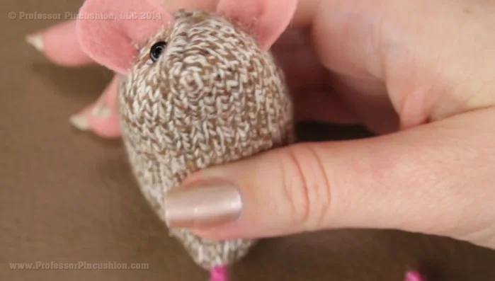 Sew on the eyes using a needle and thread. Start from underneath to hide the knot. Add the bead, sew through the fabric, pull tight to create a sunken look, and secure the knot.