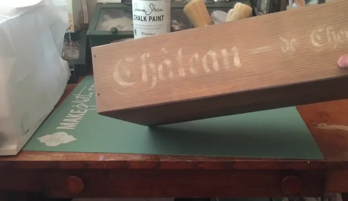 Apply Chalk Paint: Apply Annie Sloan Chalk Paint (Old White) over the stained wood and use a stencil (Chateau) to add a design. Lightly sand to distress the paint and create a vintage look.