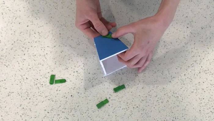 Attach the small popsicle stick pieces to the inside of the box, ensuring the elastic will hook onto them (avoid the mistake of attaching them upside down!).