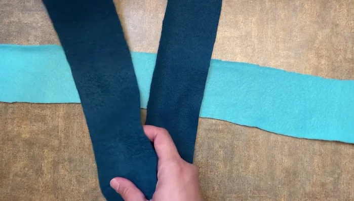 Take the leftmost piece of the horizontal fleece strip, pull it over the middle vertical piece, and then through the rightmost vertical piece to create a square knot.
