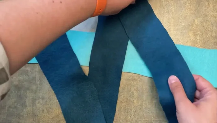 Take the leftmost piece of the horizontal fleece strip, pull it over the middle vertical piece, and then through the rightmost vertical piece to create a square knot.